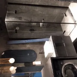 Nowoczesna łazienka w odcieniach szarości z kabiną prysznicową typu walk-in z czarnymi profilami, owalną umywalką, czarną szafką z blatem, pralką oraz dekoracyjnymi lampami wiszącymi z metalowymi...