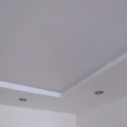 Gładki, biały sufit podwieszany z płyt karton-gips z wbudowanymi dwoma punktowymi lampami halogenowymi, wykończony listwą dekoracyjną.