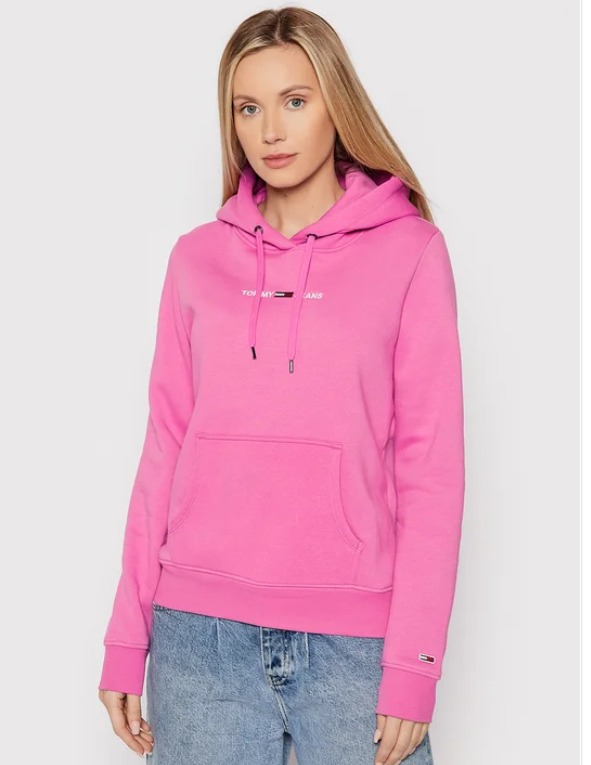Kobieta prezentuje różową bluzę z kapturem marki Tommy Jeans na jednolitym tle.