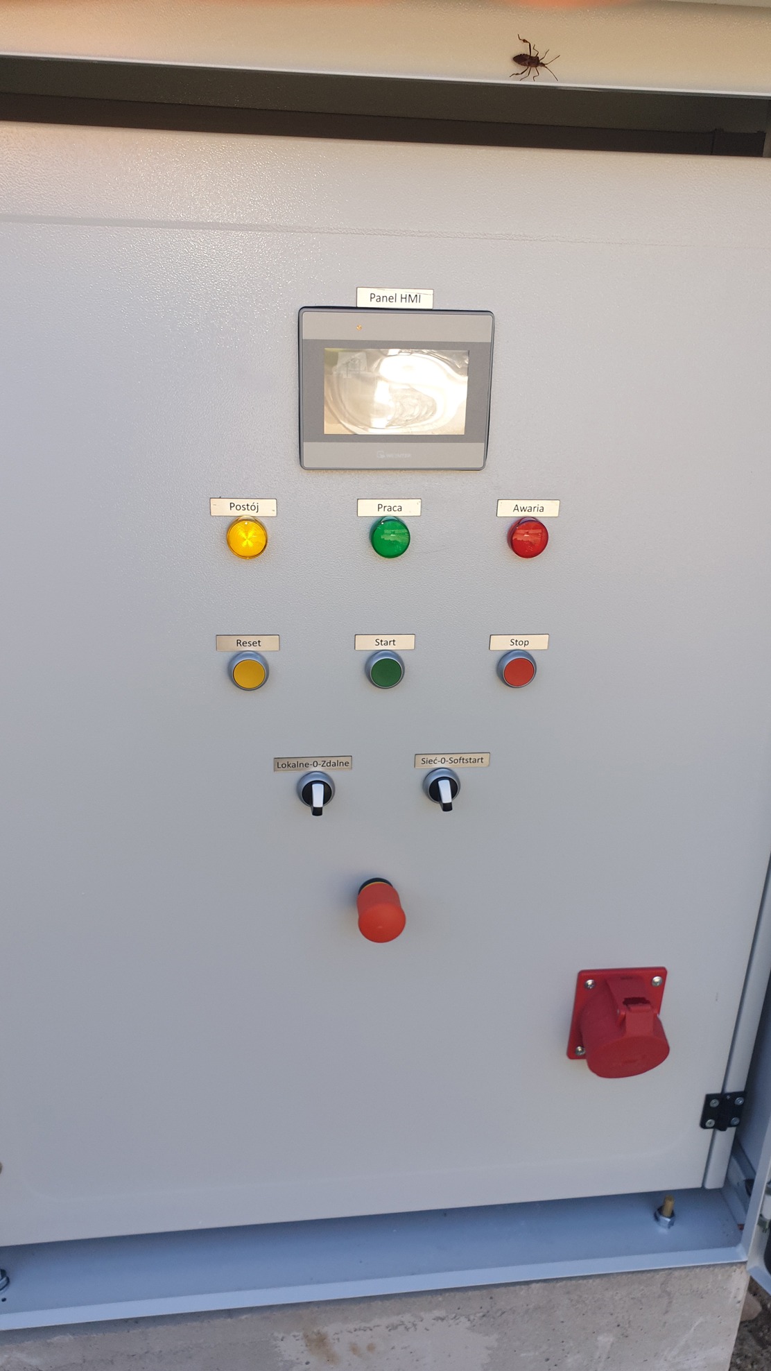 Szara elewacja rozdzielnicy zasilająco-sterowniczej z panelem HMI, przyciskami 'Postój', 'Praca', 'Awaria', 'Reset', 'Start', 'Stop' oraz przełącznikami 'Lokalne-0-Zdalne' i 'Sieć-0-Softstart'.