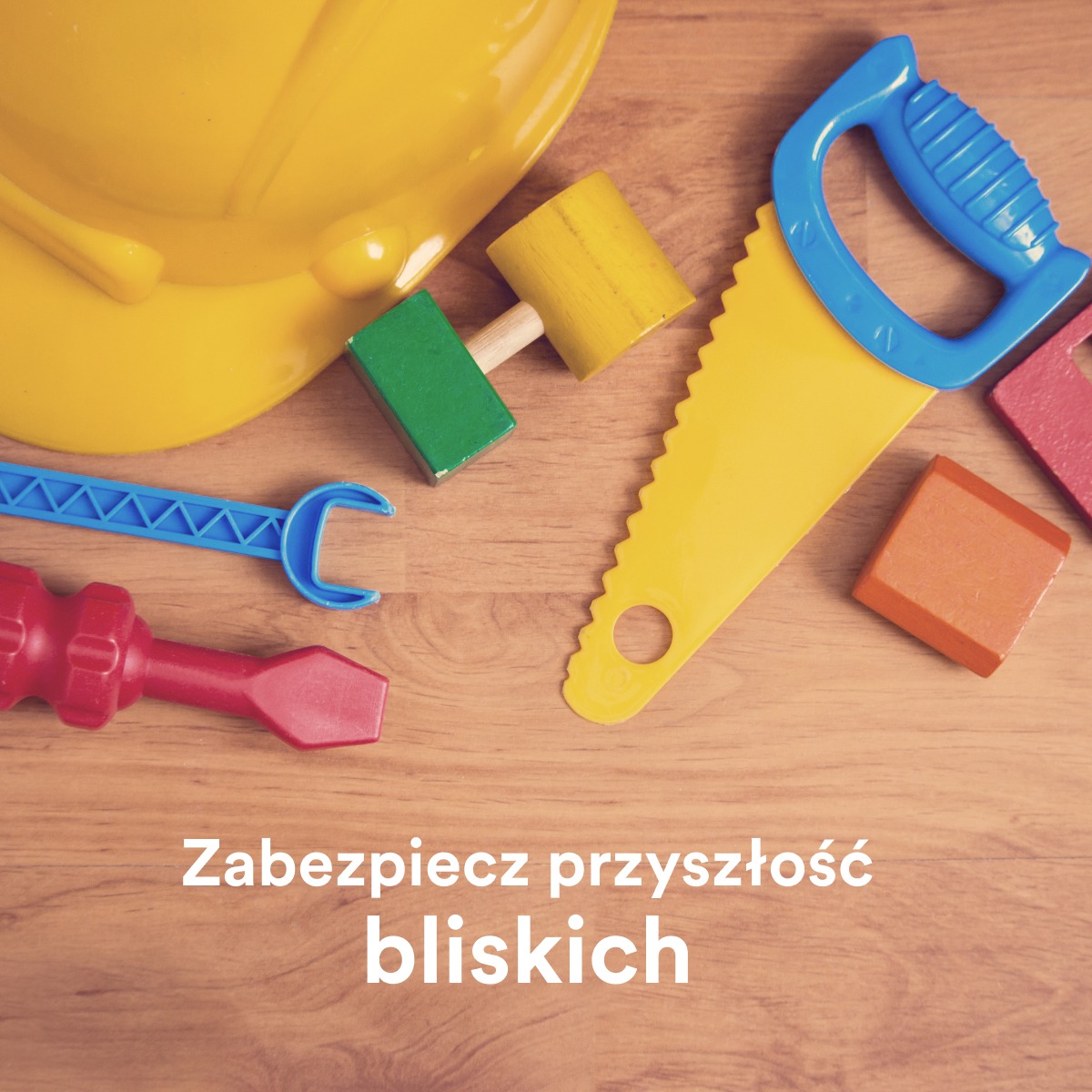 Kolorowe plastikowe zabawki narzędzia (kask, młotki, piła, klucz, śrubokręt) na drewnianym tle z napisem 'Zabezpiecz przyszłość bliskich'.