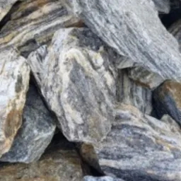 Kupa kamieni o wyraźnych szarych i brązowych pasach, ułożonych jeden na drugim, widoczna tekstura i nieregularne kształty.