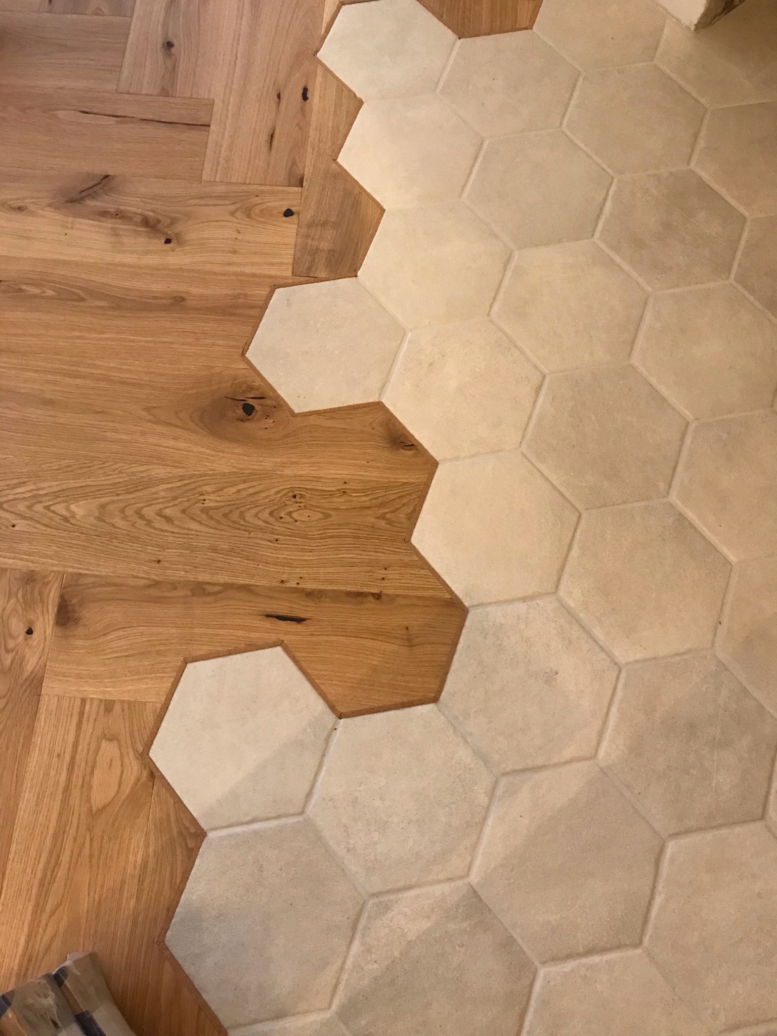 Połączenie jodełki parkietowej z jasnymi, heksagonalnymi płytkami podłogowymi, widoczne detale usłojenia drewna i fugi płytek.