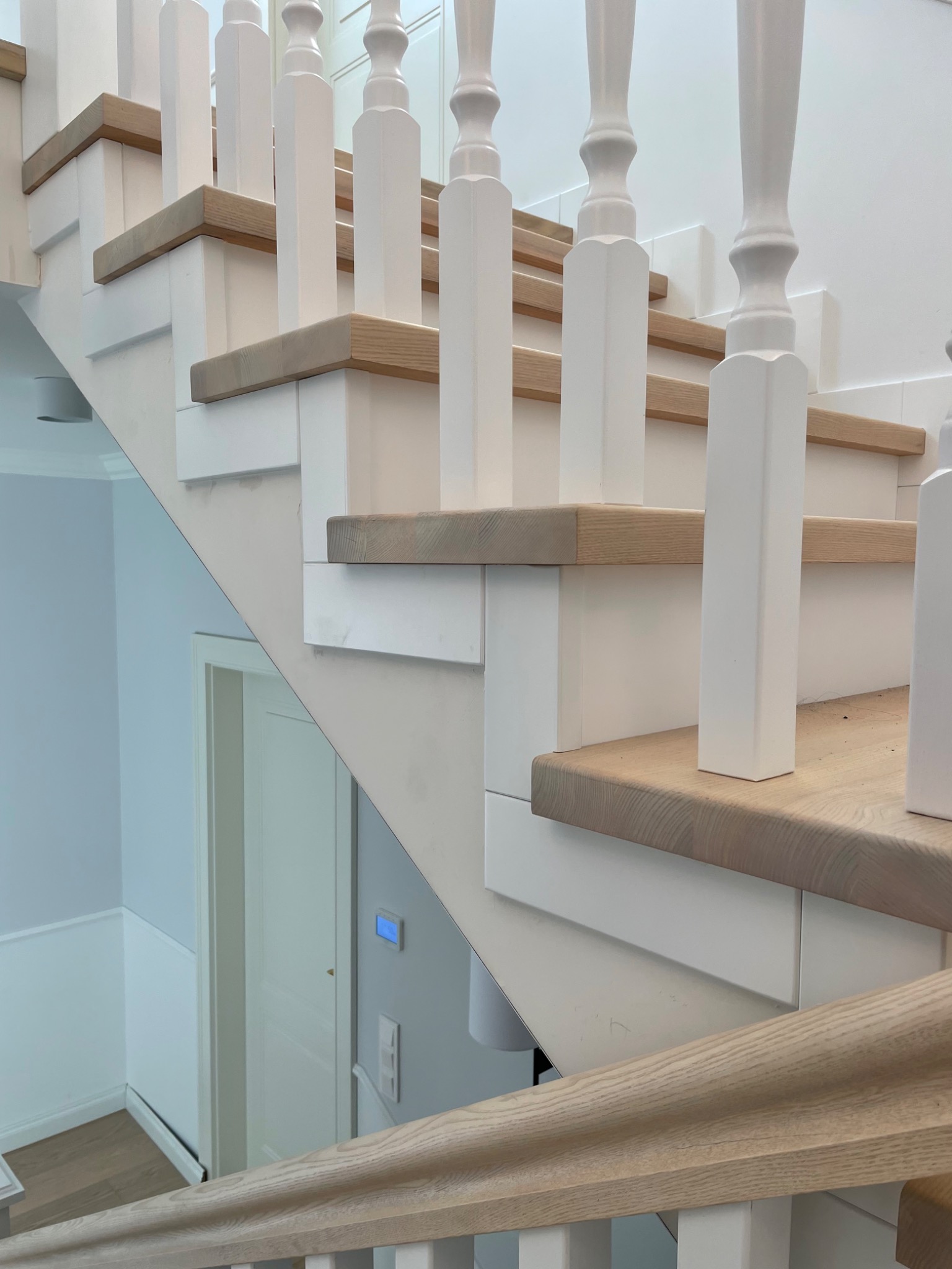 Nowoczesne schody drewniane z białymi balustradami i dębowymi stopniami, widok z dołu, minimalistyczny design i jasne kolory.
