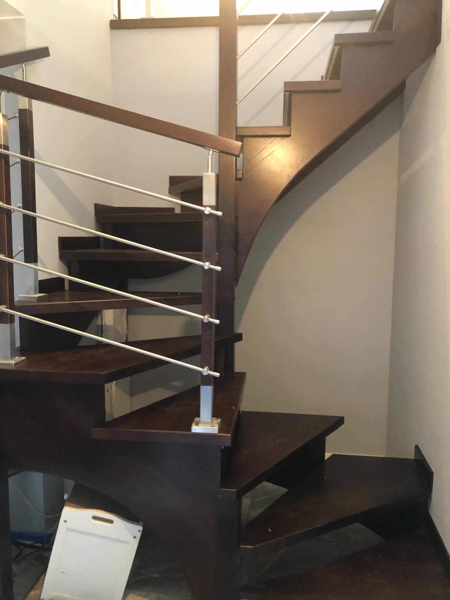 Spiralne, ciemnobrązowe stopnie z metalową balustradą w jasnym wnętrzu, widoczne od dołu, z elementami wykończeniowymi w tle.