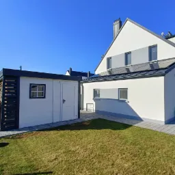 Nowoczesny dom jednorodzinny z panelami słonecznymi na dachu, widok z ogrodu w słoneczny dzień.