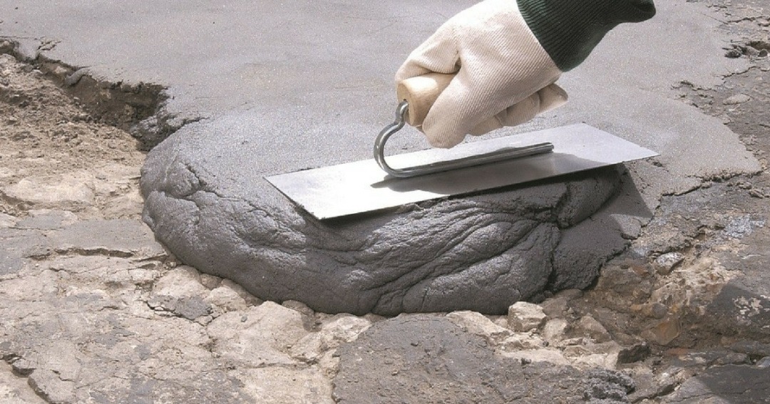 Nierówna powierzchnia z wypełnieniem zaprawą murarską, wyrównywana pacą trzymaną w rękawicy roboczej.