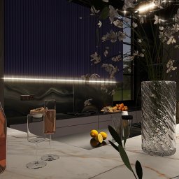 Natalia Korczyńska - Nowoczesna kuchnia z marmurowym blatem, butelką różowego wina i kwiatami w szklanym wazonie. W tle widoczna zabudowa kuchenna z oświetleniem LED i dekoracyjna ściana.