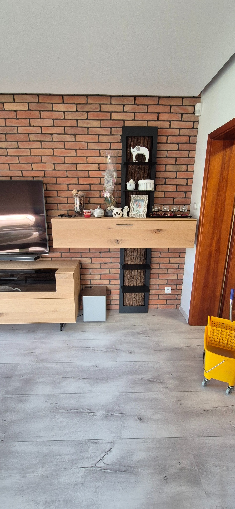 Ustawiona żółta wiadro na kółkach do sprzątania podłogi w salonie z ceglaną ścianą i drewnianymi meblami.