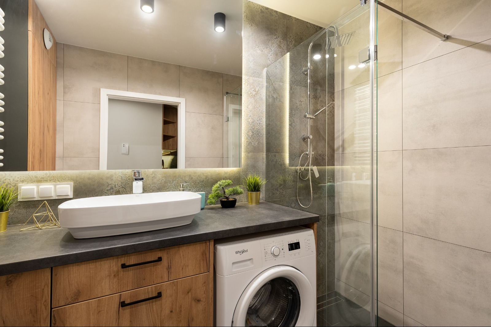 Nowoczesna łazienka z umywalką nablatową, kabiną prysznicową typu walk-in, pralką pod blatem i lustrem z podświetleniem LED.