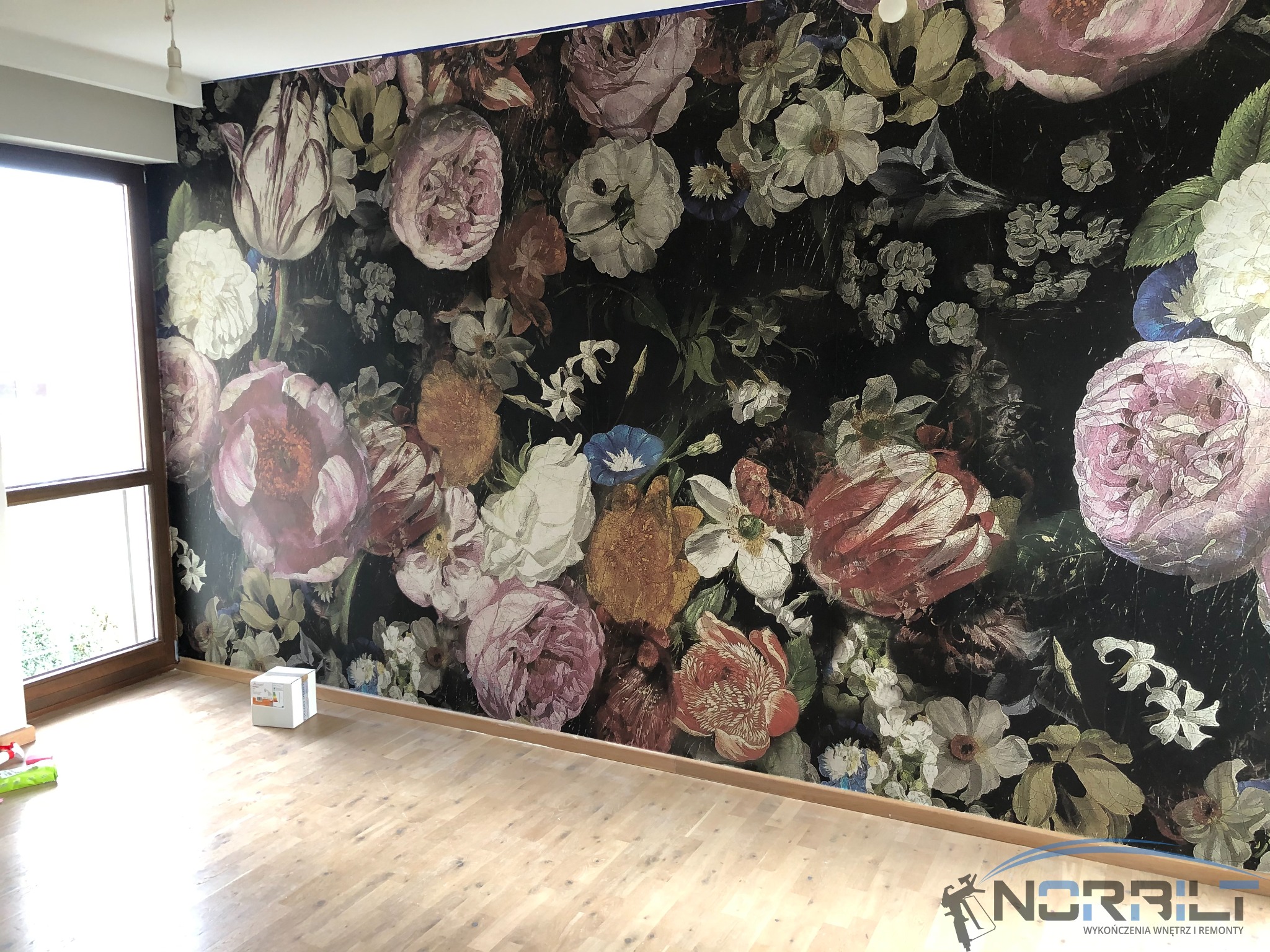 Ściana po aplikacji fototapety z motywem kwiatowym w stylu retro, widoczna drewniana podłoga i pudełko farby pod ścianą.