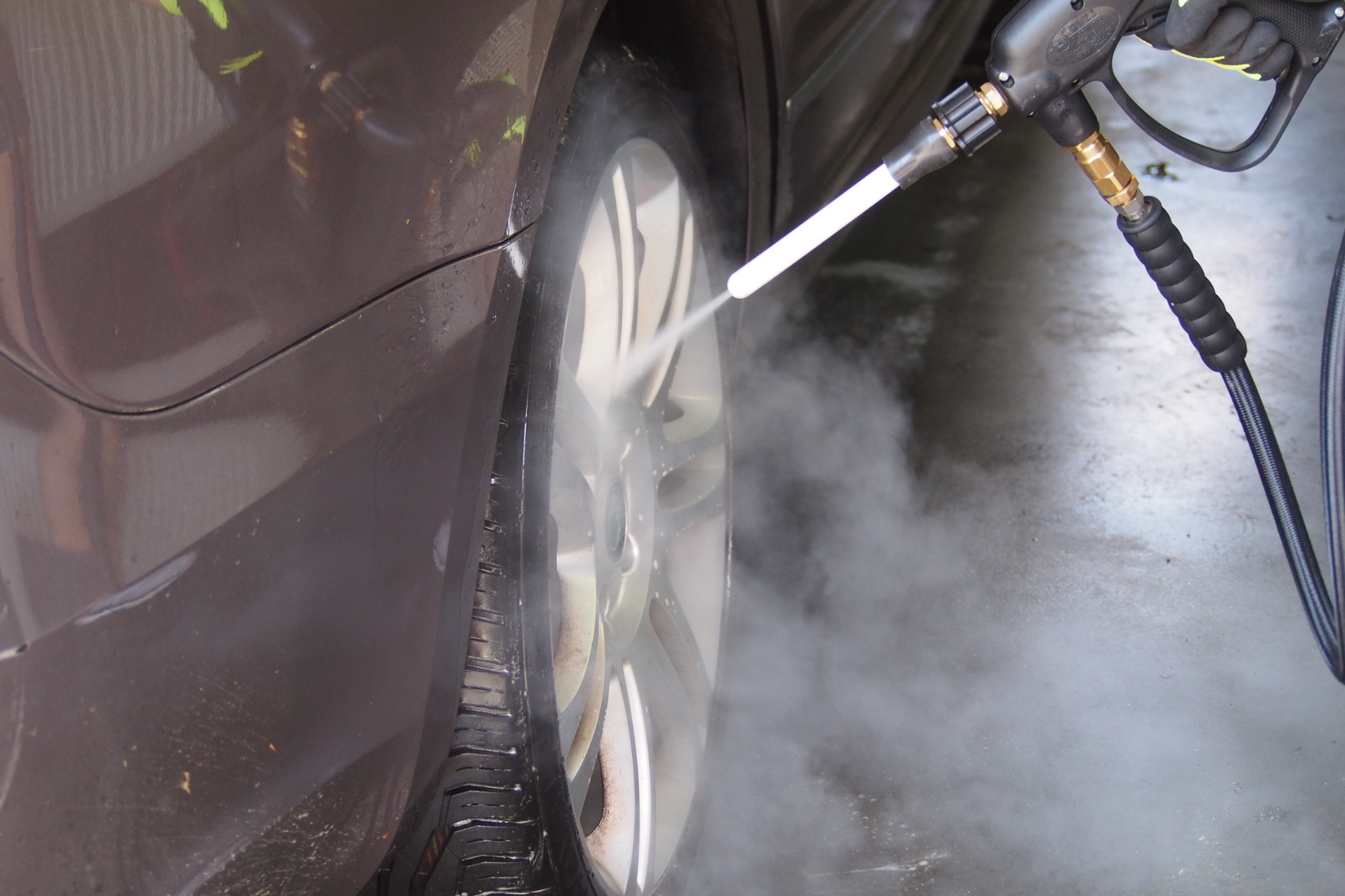 Czyszczenie felgi aluminiowej brązowego samochodu myjką ciśnieniową, widoczna piana i woda pod ciśnieniem.