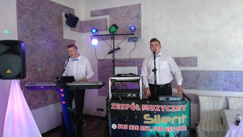 Dwóch mężczyzn w białych koszulach z muszkami występuje na weselu, jeden gra na keyboardzie Yamaha, drugi śpiewa do mikrofonu, w tle nagłośnienie i oświetlenie.