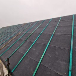 Usługi budowlane Mateusz Schröder - Widok z góry na dach domu w trakcie budowy, pokryty czarną membraną i łatami zaimpregnowanymi na zielono, przygotowany pod pokrycie dachowe.