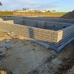 Usługi budowlane Mateusz Schröder - Fundamenty domu z betonu komórkowego, widok z góry na częściowo ukończoną konstrukcję. W tle dom w budowie i sterta ziemi.