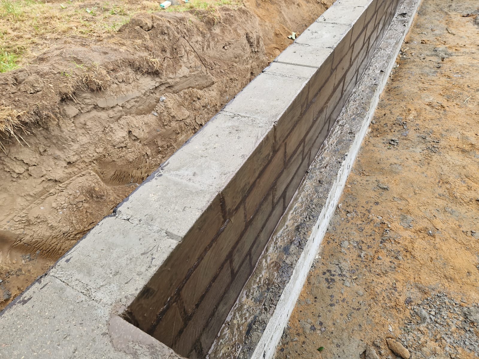 Wykop pod fundament z częściowo wymurowaną ścianą z betonowych bloczków, widoczna wilgoć na świeżo położonej zaprawie.