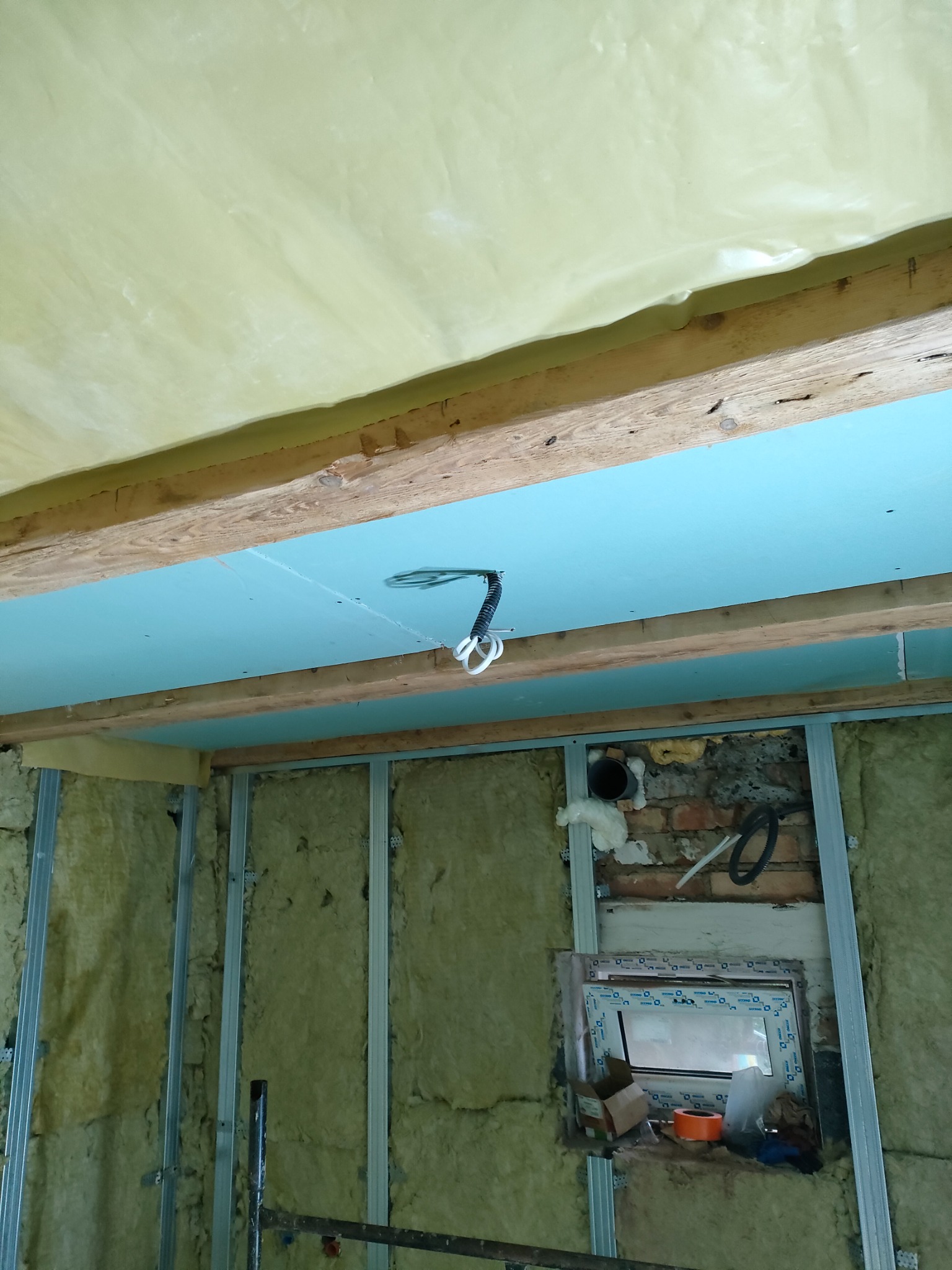 Montaż izolacji i płyt kartonowo-gipsowych w Żarowie: widok na sufit z zamontowanymi płytami w kolorze błękitnym, drewniane belki konstrukcyjne, folia ochronna i ściany z izolacją z wełny...