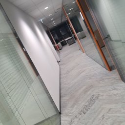 JSK Electric - Długi korytarz biurowy z przeszklonymi ścianami, oświetlony panelami LED w suficie podwieszanym. Widoczny system detekcji pożaru.