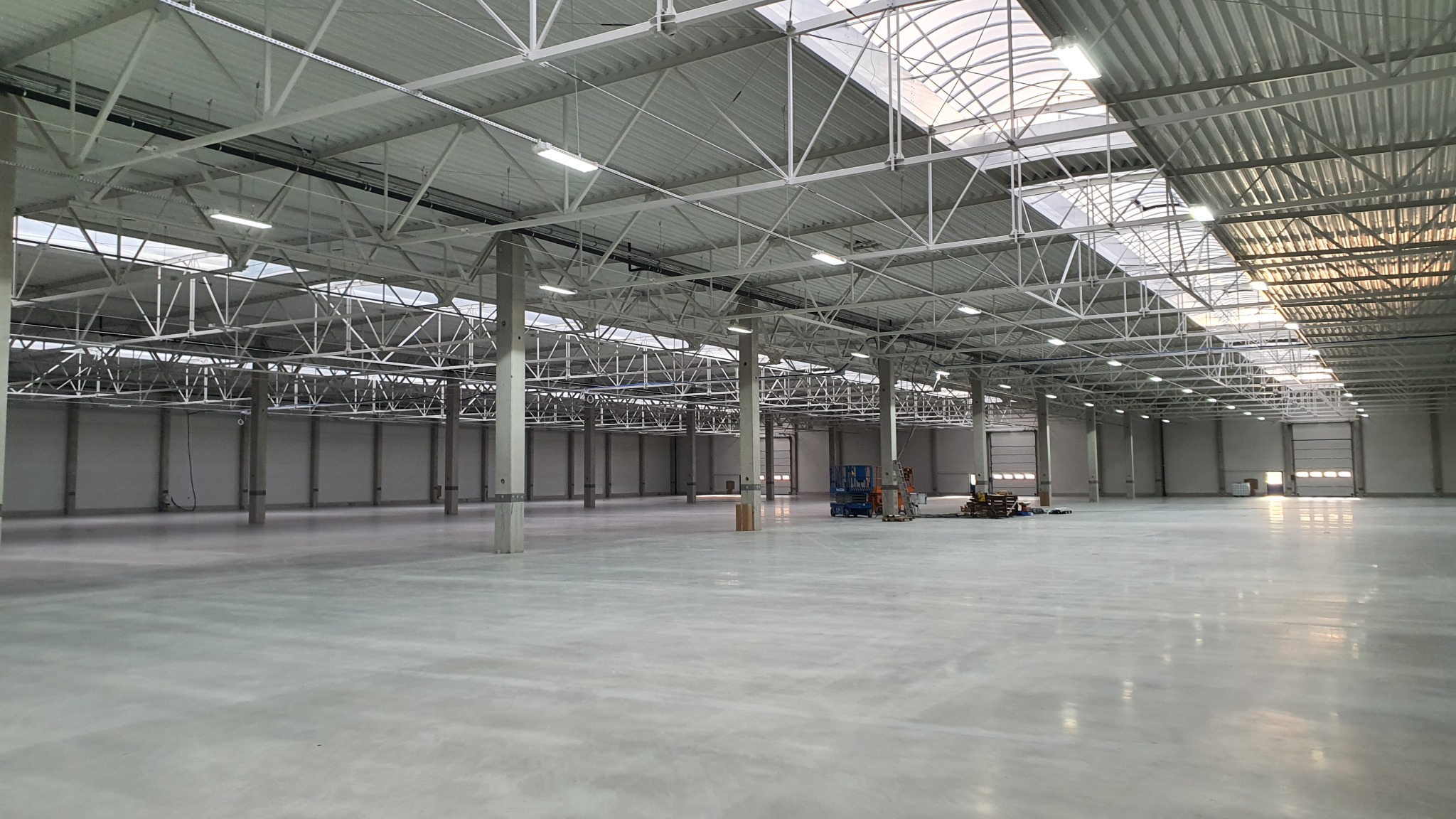 Przestronna, pusta hala magazynowa we Wrocławiu z widoczną konstrukcją stalową dachu, oświetleniem LED i betonową posadzką. W tle widoczne bramy wjazdowe.