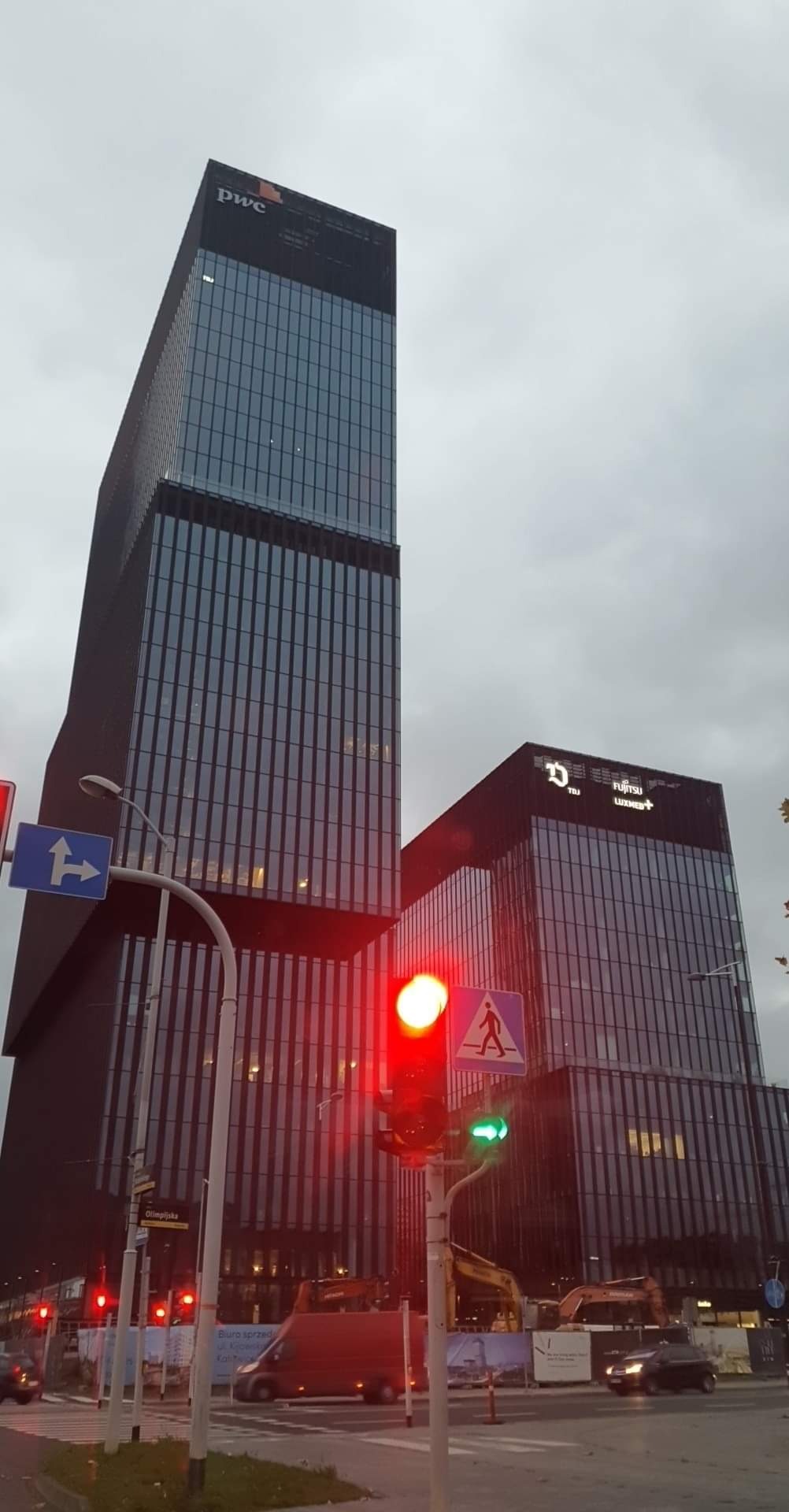 Widok na nowoczesne biurowce w pochmurny dzień, z sygnalizacją świetlną na pierwszym planie i budową w tle.