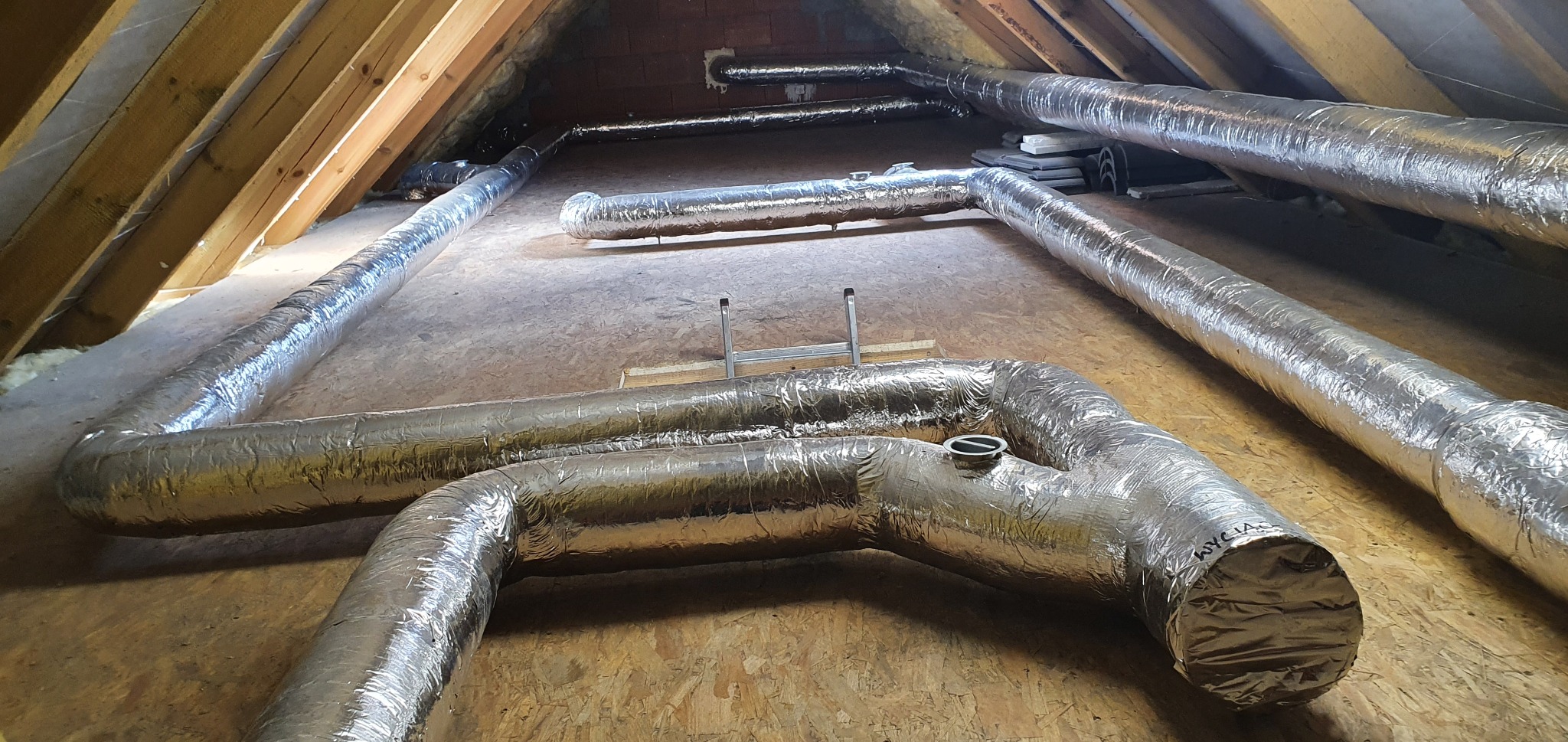 System izolowanych rur wentylacyjnych ułożonych w przestrzeni poddasza, widoczne elementy mocujące i łączenia.