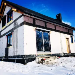 Dom w trakcie budowy, widoczne okna z zamontowanymi roletami zewnętrznymi, ośnieżony teren.