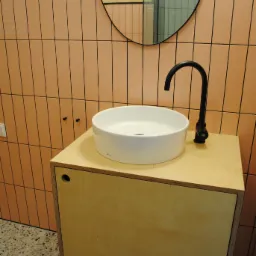 Nowoczesna łazienka z umywalką nablatową na drewnianej szafce, czarna bateria i owalne lustro na tle różowych płytek.