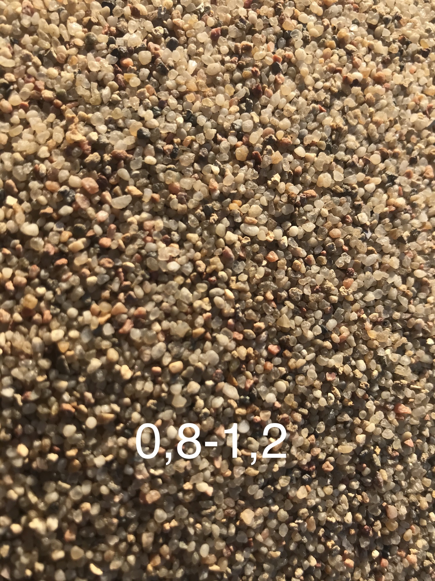 Detale ziaren kruszywa o frakcji 0,8-1,2 mm, w odcieniach beżu i brązu, oświetlone naturalnym światłem.