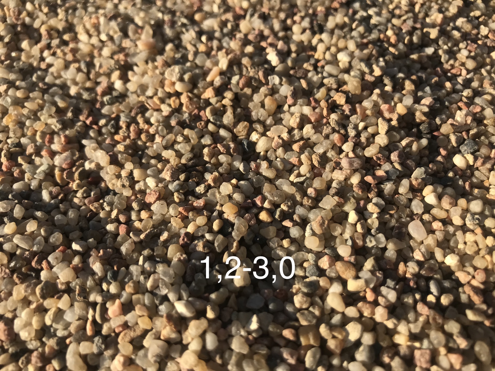 Drobny, okrągły materiał budowlany w odcieniach beżu i brązu, oświetlony z góry, z widocznym gradientem światła i cienia.