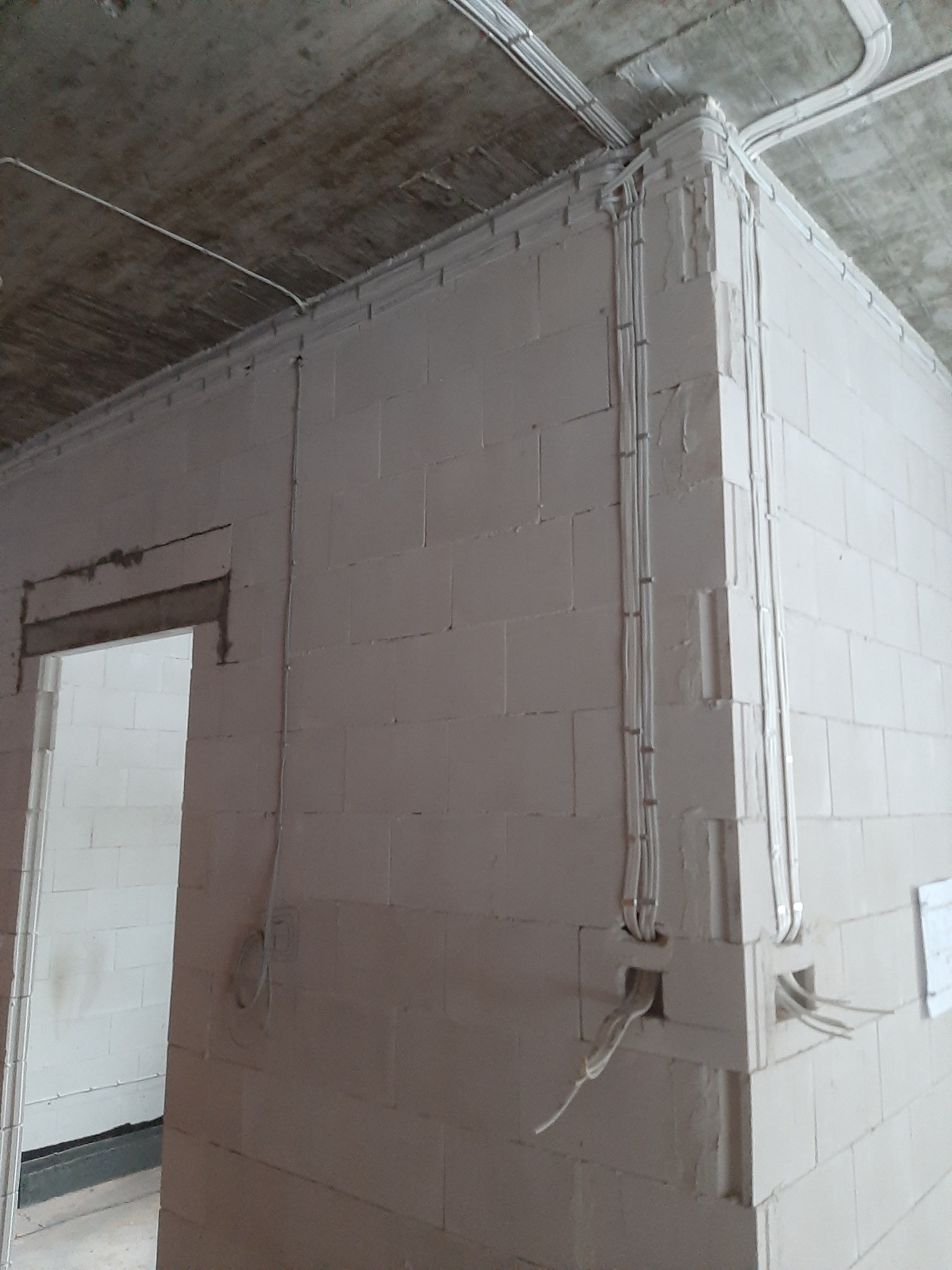 Surowe wnętrze w trakcie prac wykończeniowych: białe ściany z betonu komórkowego z widocznymi przewodami w peszlach prowadzonymi po powierzchni, surowy betonowy strop.