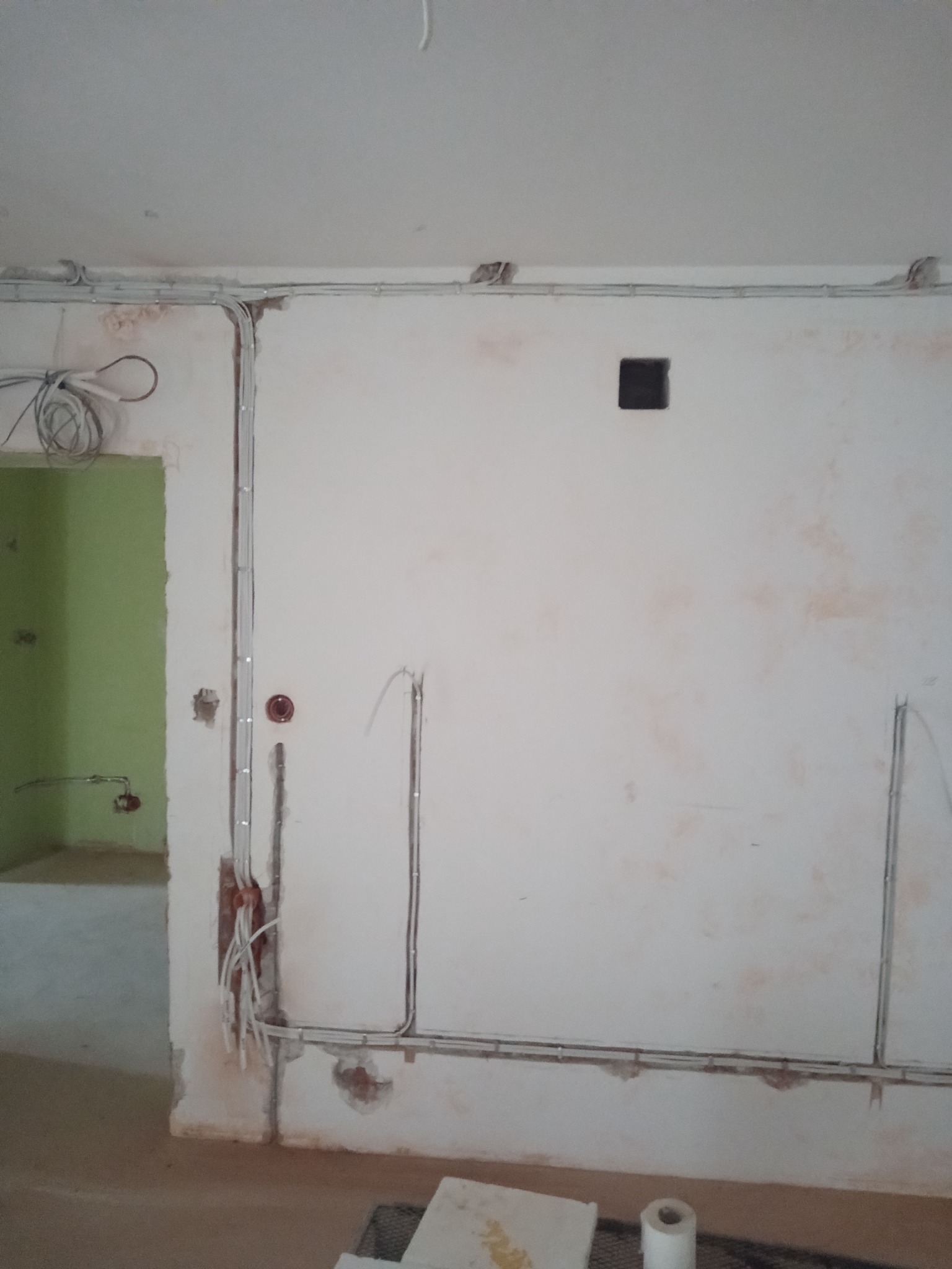 Wnętrze w trakcie remontu z widocznymi przewodami elektrycznymi prowadzonymi po ścianach i suficie, puszka elektryczna w ścianie, widoczne kable wystające ze ściany, surowy stan wykończenia.