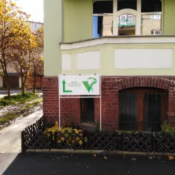 Zewnętrzny widok budynku z szyldem informującym o gabinecie na Zamenhofa, z zielonym logo w kształcie węża Eskulapa i strzałki w górę.