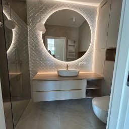 K&K Remonty Spółka z ograniczona odpowiedzialnoscia - Nowoczesna łazienka z okrągłym lustrem podświetlanym LED, umywalką nablatową i płytkami w kształcie rybiej łuski. Minimalistyczne szafki i szara podłoga.