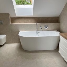 K&K Remonty Spółka z ograniczona odpowiedzialnoscia - Nowoczesna łazienka na poddaszu z wolnostojącą wanną, beżowymi płytkami i oknem dachowym. Minimalistyczny design, jasne wnętrze.