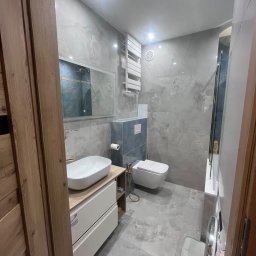 K&K Remonty Spółka z ograniczona odpowiedzialnoscia - Stylowa łazienka w szarościach: marmurowe płytki, podwieszana toaleta, umywalka nablatowa z złotą armaturą i grzejnik drabinkowy. Nowoczesne oświetlenie.