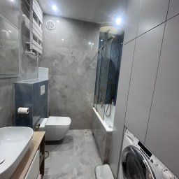 K&K Remonty Spółka z ograniczona odpowiedzialnoscia - Nowoczesna łazienka w szarościach z marmurowymi płytkami, kabiną prysznicową nad wanną i pralką. Minimalistyczny design z podwieszaną toaletą i grzejnikiem drabinkowym.