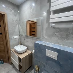 K&K Remonty Spółka z ograniczona odpowiedzialnoscia - Nowoczesna łazienka z umywalką nablatową, lustrem z podświetleniem LED i grzejnikiem drabinkowym. Szare płytki imitujące marmur i akcenty w kolorze niebieskim.