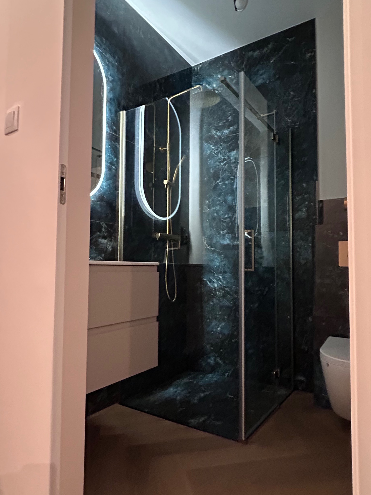 Nowoczesna łazienka z kabiną prysznicową typu walk-in, umywalką z szafką i toaletą. Ściany wykończone płytkami imitującymi marmur w odcieniach granatu i złota.