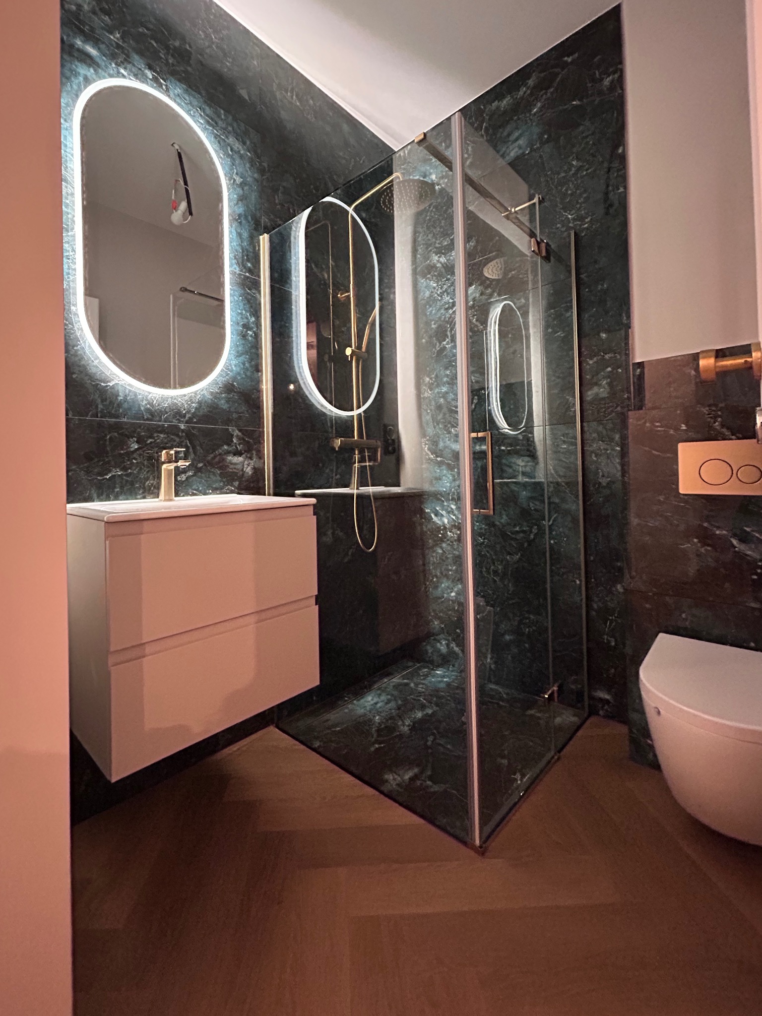 Nowoczesna łazienka z kabiną prysznicową typu walk-in, umywalką z szafką i podświetlanym lustrem na tle ściany z płytek imitujących marmur.