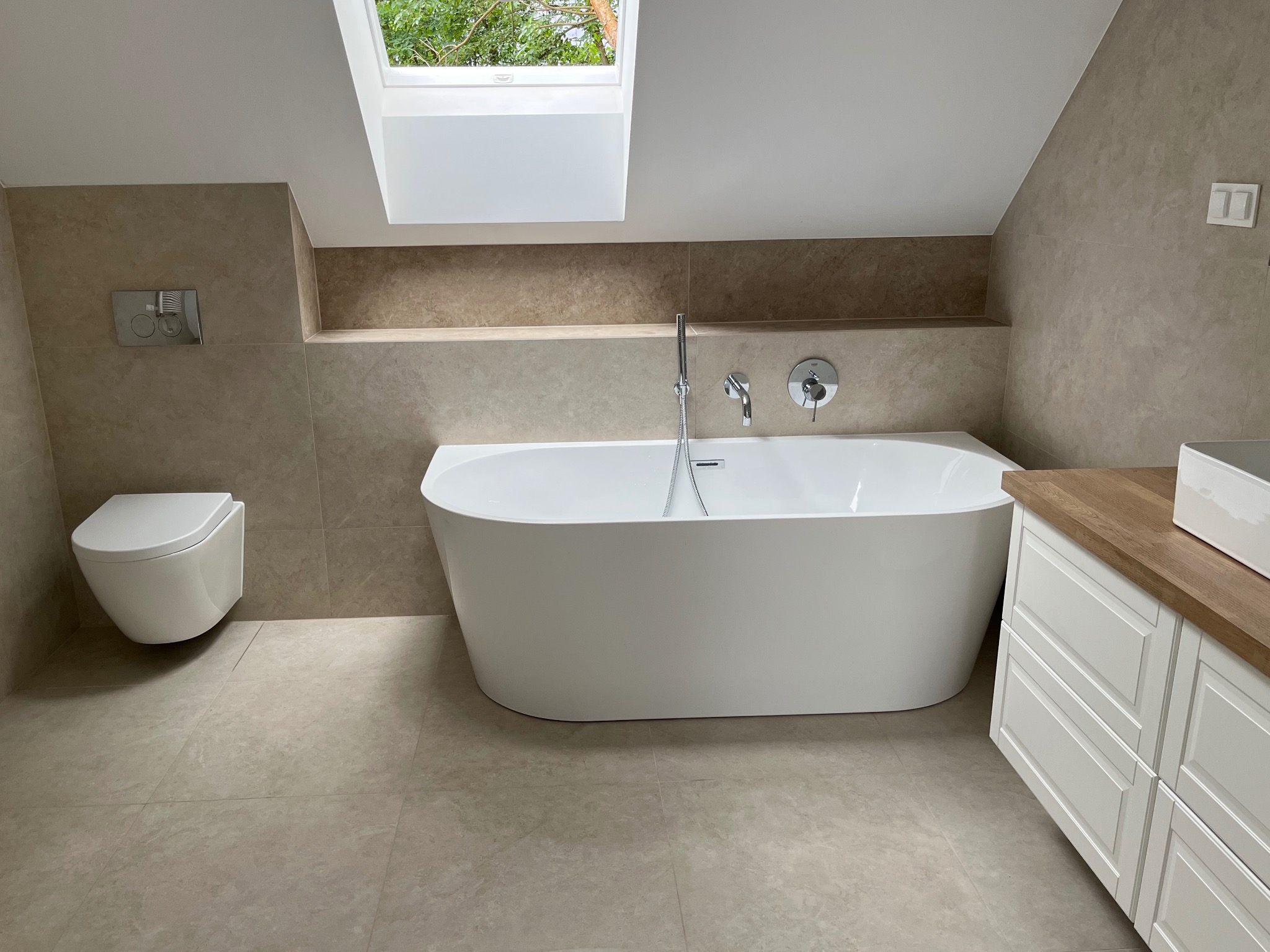 Nowoczesna łazienka na poddaszu z wolnostojącą wanną, beżowymi płytkami i oknem dachowym. Minimalistyczny design, jasne wnętrze.