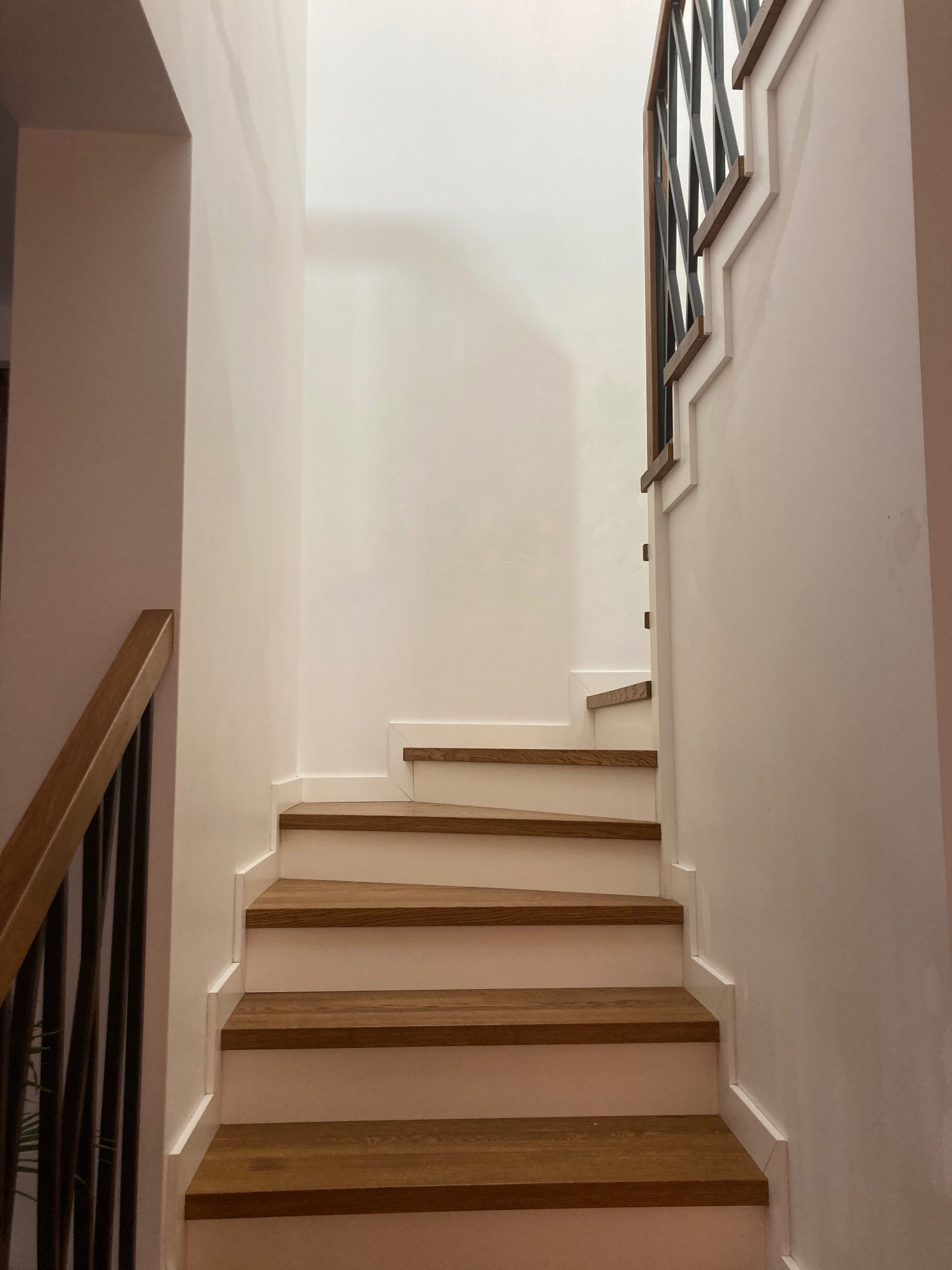 Nowoczesne schody drewniane z białymi podstopnicami i metalową balustradą w jasnym wnętrzu. Minimalistyczny design, eleganckie wykończenie.