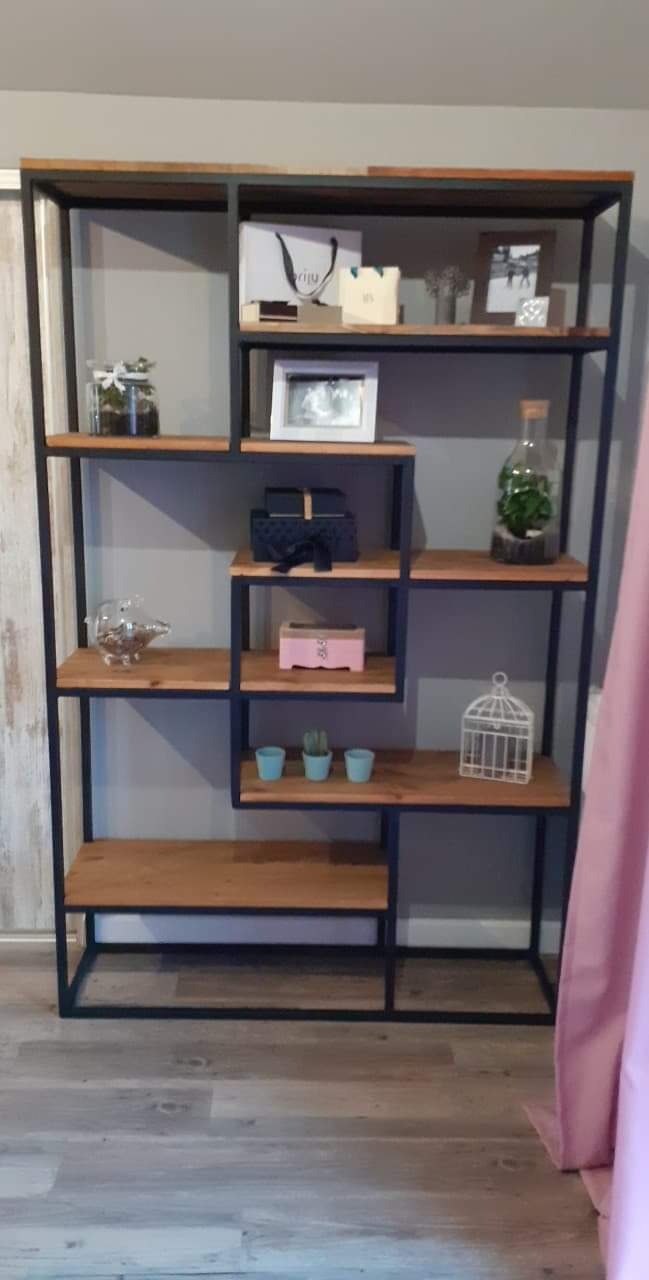 Ręcznie wykonany regał z czarnego metalu i drewnianych półek, asymetryczny układ, dekoracyjne przedmioty na półkach, widoczny fragment zasłony.