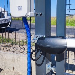 P.H.U TECH-MIKI - Zamontowany napęd do bramy z niebieską rurką osłonową. Widoczna skrzynka sterująca marki Roger na słupku ogrodzenia panelowego.
