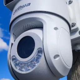 Biała kamera obrotowa Dahua z diodami IR, zamontowana na drewnianym słupie, z widocznym fragmentem drabiny i błękitnym niebem w tle.