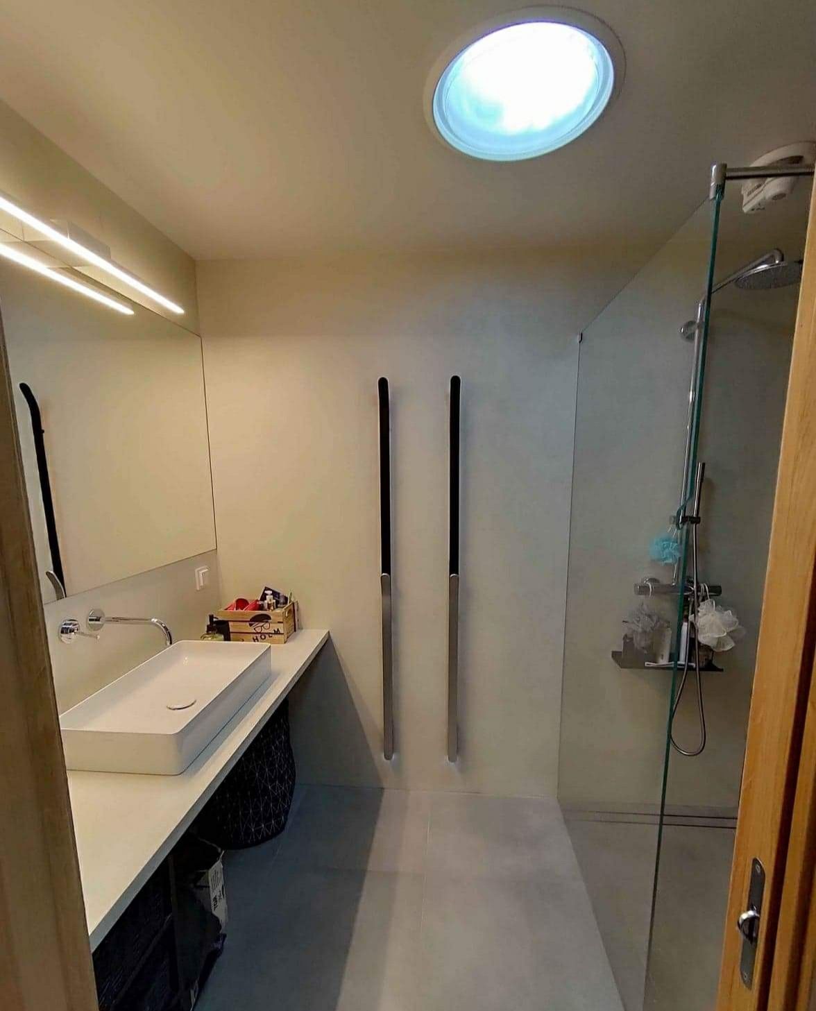 Nowoczesna łazienka z prostokątną umywalką nablatową, szklaną kabiną prysznicową i okrągłym świetlikiem w suficie.