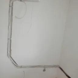 Instalacja przewodów wentylacyjnych w bruzdach ściennych, widoczne mocowania i wystające kable, surowy stan wykończenia wnętrza.