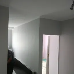 Wnętrze po odświeżeniu koloru ścian na szaro, widoczne listwy przypodłogowe, częściowo widoczna osoba i panele podłogowe w tle.