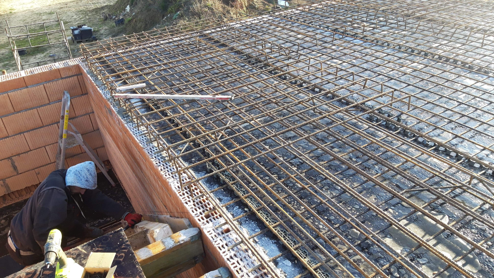 Zbrojenie stropu na murze z cegły, widoczny poziomica i pracownik w trakcie montażu, przygotowanie do wylewki betonu.