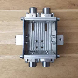 Metalowa rama z elementami cylindrycznymi, połączona śrubami, widoczna z góry na drewnianym tle, prawdopodobnie część maszyny.