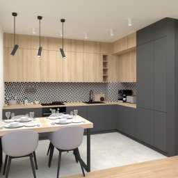 EN.concept Jolanta Grzelak - Nowoczesna kuchnia z drewnianymi szafkami górnymi, szarymi szafkami dolnymi i geometrycznym wzorem płytek na ścianie nad blatem, stół z nakryciem dla dwóch osób przy oknie.